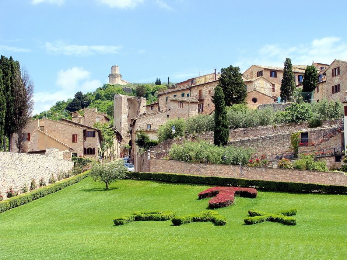 Vista do Jardim da Basá¡lica de Sáúo Francisco de Assis, com casas ao redor. Ao fundo e no alto, parte da muralha que circunda o burgo.